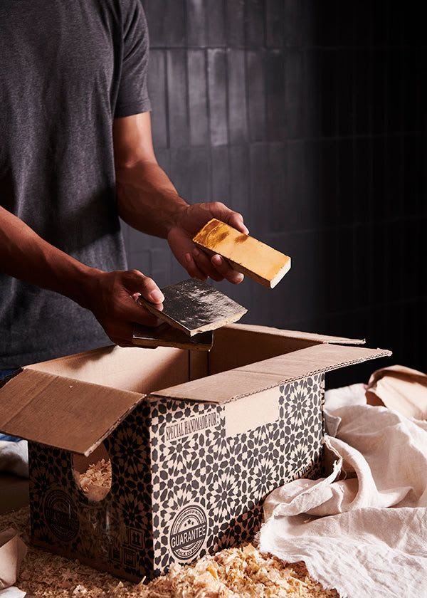 Master artisan carefully packing handmade Moroccan Zellige tiles into a branded ZELTILE shipping box